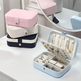 جلوی میز آرایش آیینه دار سه رنگ مشکی سفید و صورتی روی هم چیدمان شدن و در کنارشون جعبه آبی رنگ جواهرات با درب باز