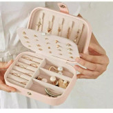 دست یه خانم با لیاس سفید که جعبه جواهر کرم رنگ رو با چیدمان جواهر داخلش باز کرده