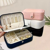 جعبه جواهرات مسافرتی مشکی به صورت باز شده و چیدمان جواهرات و در زمینه جعبه صورتی و سفید و مشکی روی هم چیدمان شدن